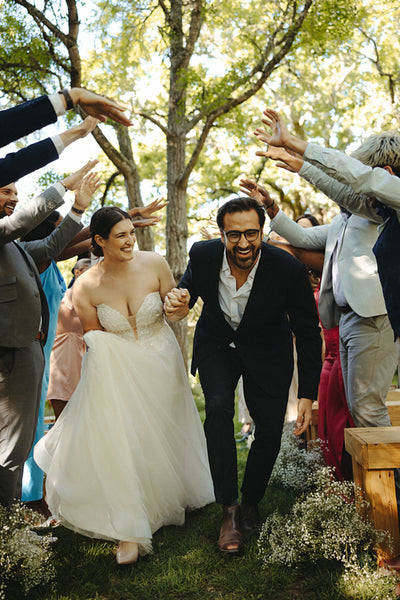 Happy wedding couple walking through joyful guests in outdoor celebration