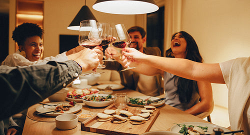 Friends toasting wine glasses during a dinner at a cozy home night