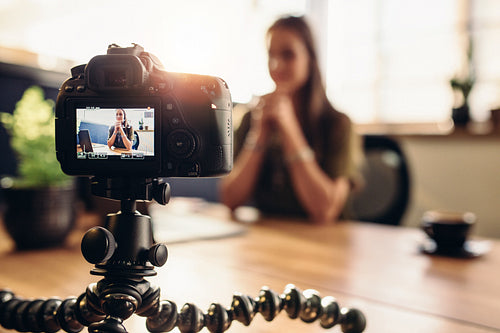 Digital camera on flexible tripod recording a video of woman at desk.