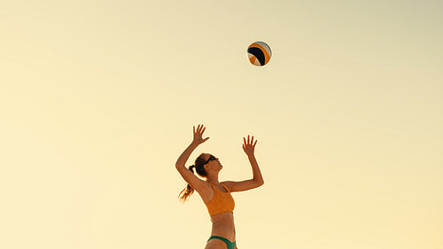 Professional female volleyball player blocking a ball at sunset