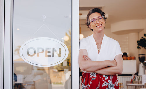 Happy coffee shop owner smiling while standing at the doorway of her newly opened cafe