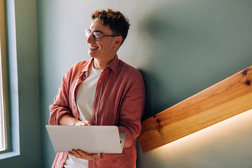 Smiling man using a laptop while leaning on a staircase indoors