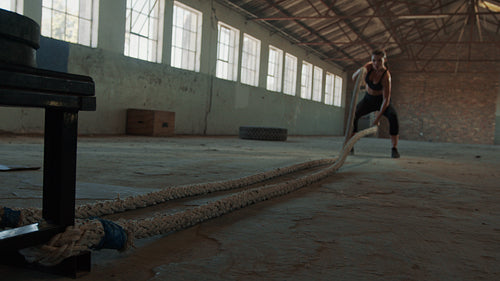 Tough woman exercising with battle rope in gym