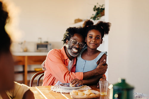 Mature dad holding his daughter at breakfast, with Brazilian cheese bread rolls on the table