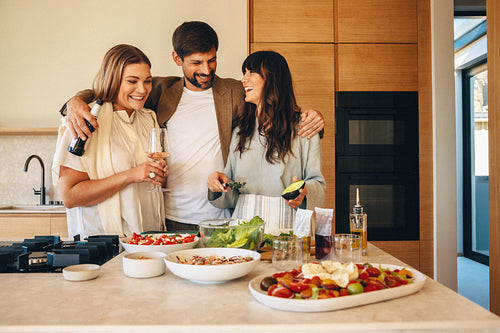Three friends cooking together and enjoying drinks in a modern kitchen