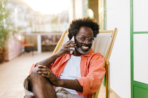 Cheerful mature black man having a relaxing phone call outdoors on the patio