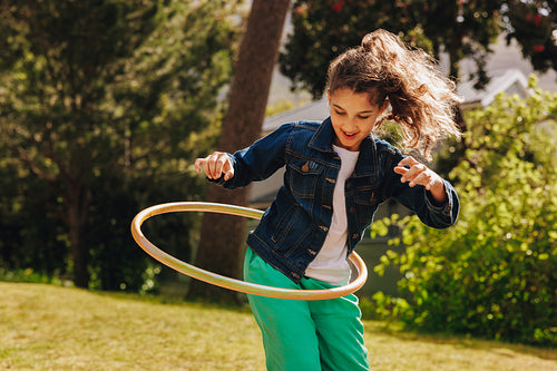 Girl playing with a hula hoop outdoors on a bright sunny day