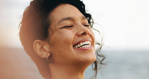 Close-up portrait of a carefree woman with wavy hair smiling at the seaside during dusk