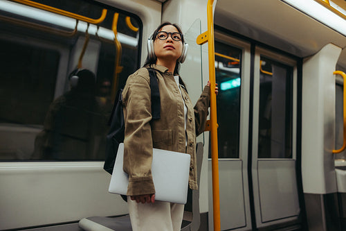 Commuter woman on train holding laptop and headphones