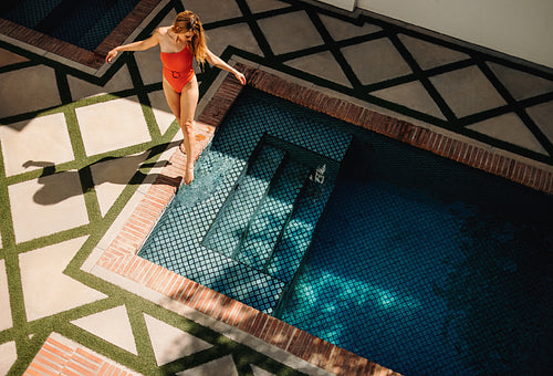 Aerial view of a young woman standing next to a pool in red swim