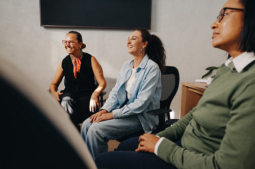 Three female coworkers engaged in discussion with smiles in an office setting