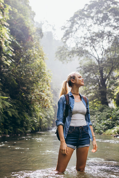 Female hiker crossing the forest creek