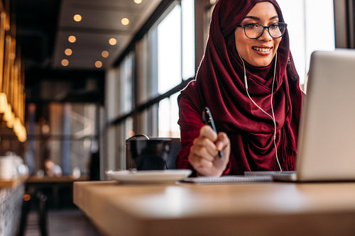 Female in hijab at cafe having video conference on her laptop