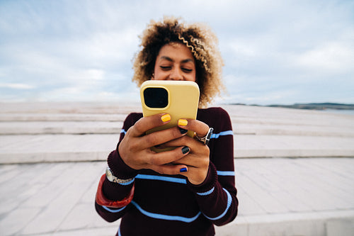 Smiling woman using smartphone outdoors at waterfront