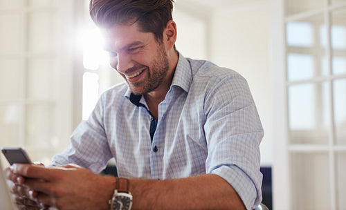 Happy young man using mobile phone at home