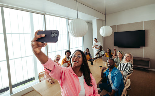 Marketing team taking a group selfie around a conference table during a meeting in a modern office setting