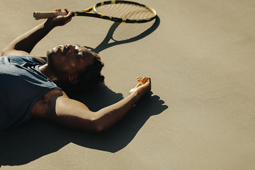 Exhausted tennis player laying down on court in sunlight