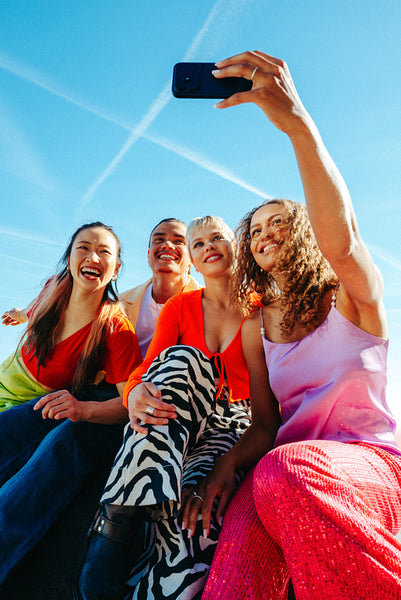 Sharing friends raise a smartphone for a selfie outdoors against blue sky