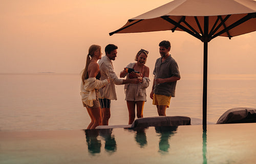 Friends pouring champagne at sunset near pool on a luxury vacation