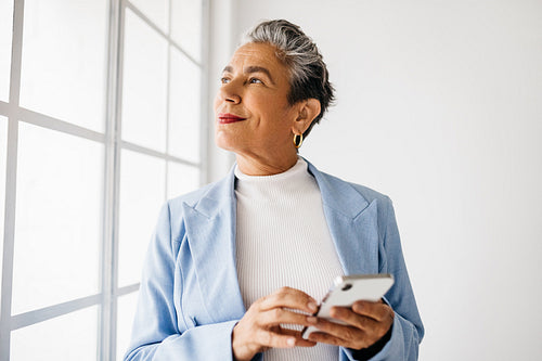 Thoughtful business woman holding a mobile phone in her office
