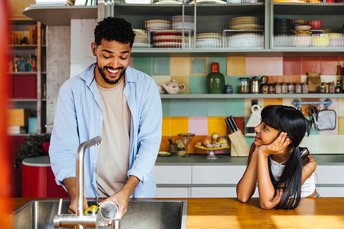 Father washing dishes while daughter watches him in a colorful kitchen