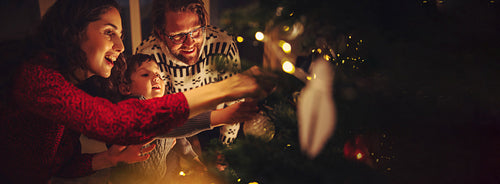 Happy family with mother, father, and child decorate Christmas tree in a cozy warm family home during winter holidays