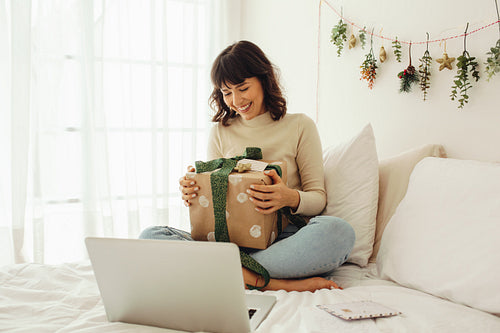 Woman sitting on bed with christmas presents doing a video call