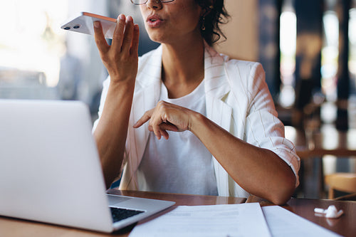 Businesswoman dictating a voice memo on smartphone while working at a cafe