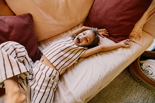 Playful girl stretching on couch in striped pajamas