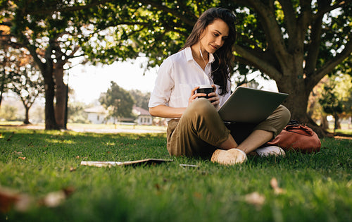 Woman at park with coffee watching video on laptop