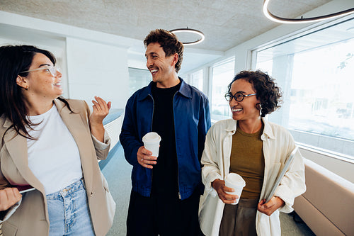Three professionals chat and share coffee in hallway