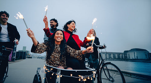 Friends enjoying an evening celebration with sparklers and bicycles by a waterfront