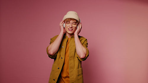 Energetic young man listening music with headphones on pink background