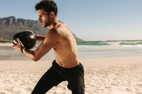 Man training at the beach using a medicine ball