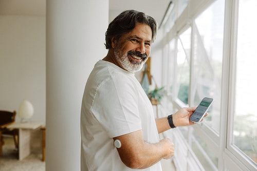 Senior man checks glucose monitor on smartphone at home