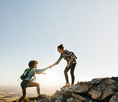 Female friends hiking help each other in mountains