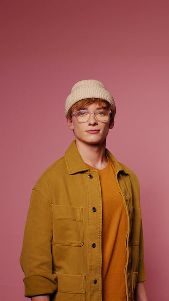 Confident young man posing in beanie and glasses against pink backdrop