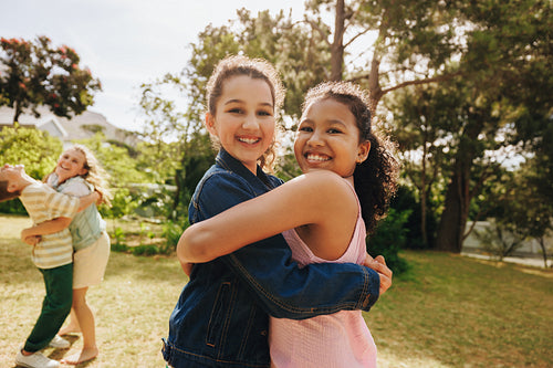 Two friends hugging outdoors on a sunny day with laughter in the background