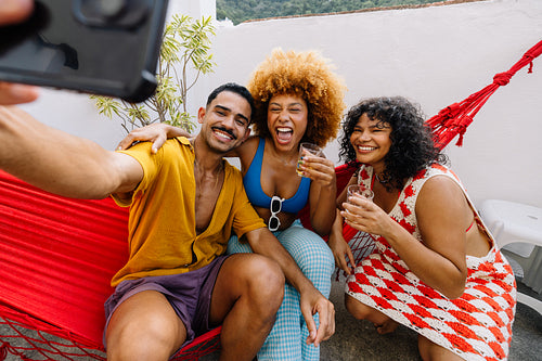 Group of Brazilian friends taking a cheerful selfie on a rooftop hammock
