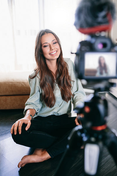 Beautiful girl recording video on tripod camera in her living room.