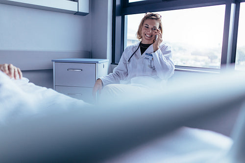 Happy female doctor sitting in hospital room and making a phone call