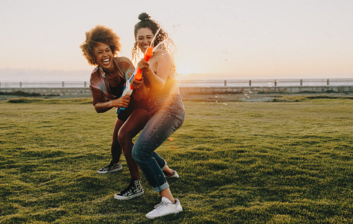 Young female friends enjoying summer fun with water guns in a park