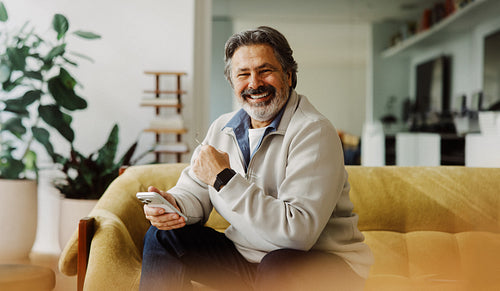 Senior man uses a smartphone while relaxing at home