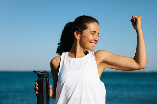 Smiling woman outdoors flexing her arm holding a water bottle