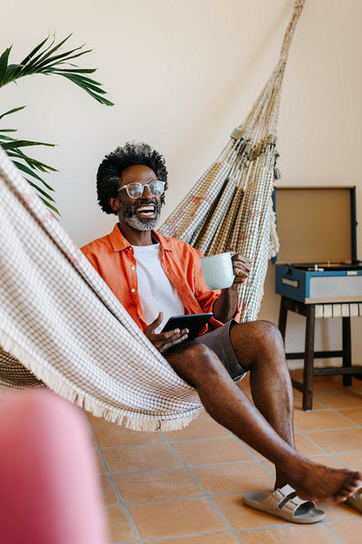 Mature black man relaxing in a hammock with a tablet and hot coffee