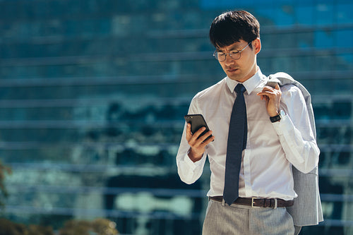 Businessman walking outdoors using his smart phone