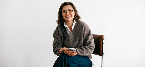 Professional woman portrait with smartphone sitting on chair in studio