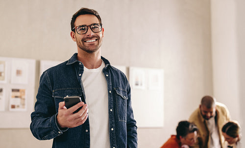 Smiling businessman holding a smartphone in an office