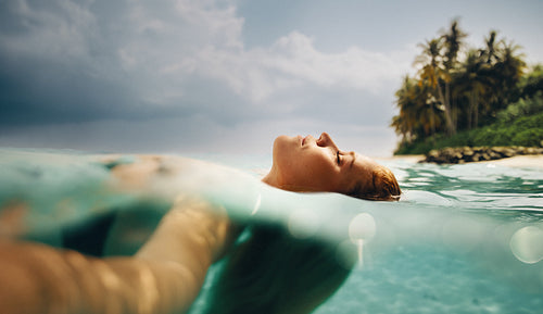 Woman relaxing in tropical ocean water near a palm tree lined beach
