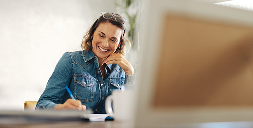 Happy businesswoman writing in her work diary at her office desk